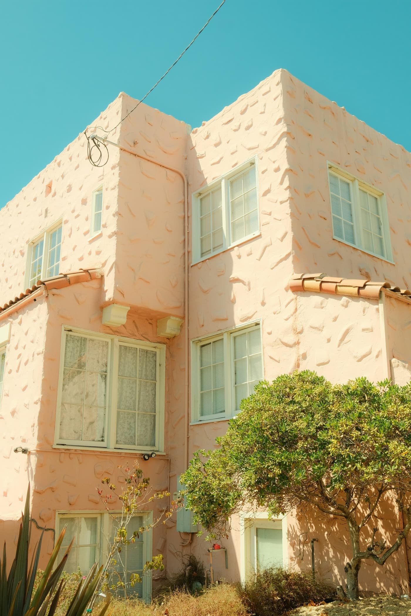 A two-storey pink stucco apartment building with white sash windows and a tiled roof edge, under a clear blue sky.
