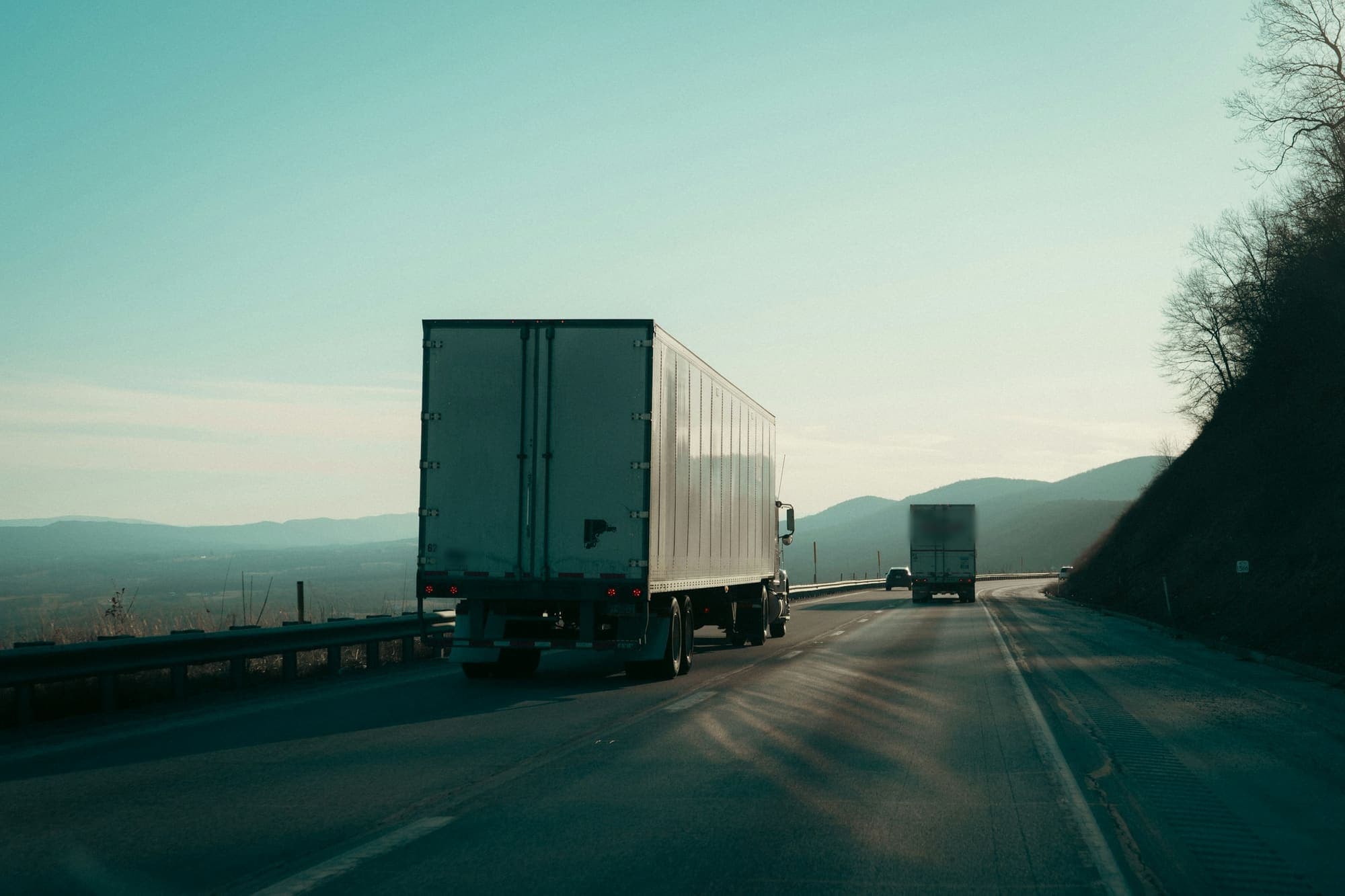 A box trailer heading along a highway in late afternoon light, with hills behind