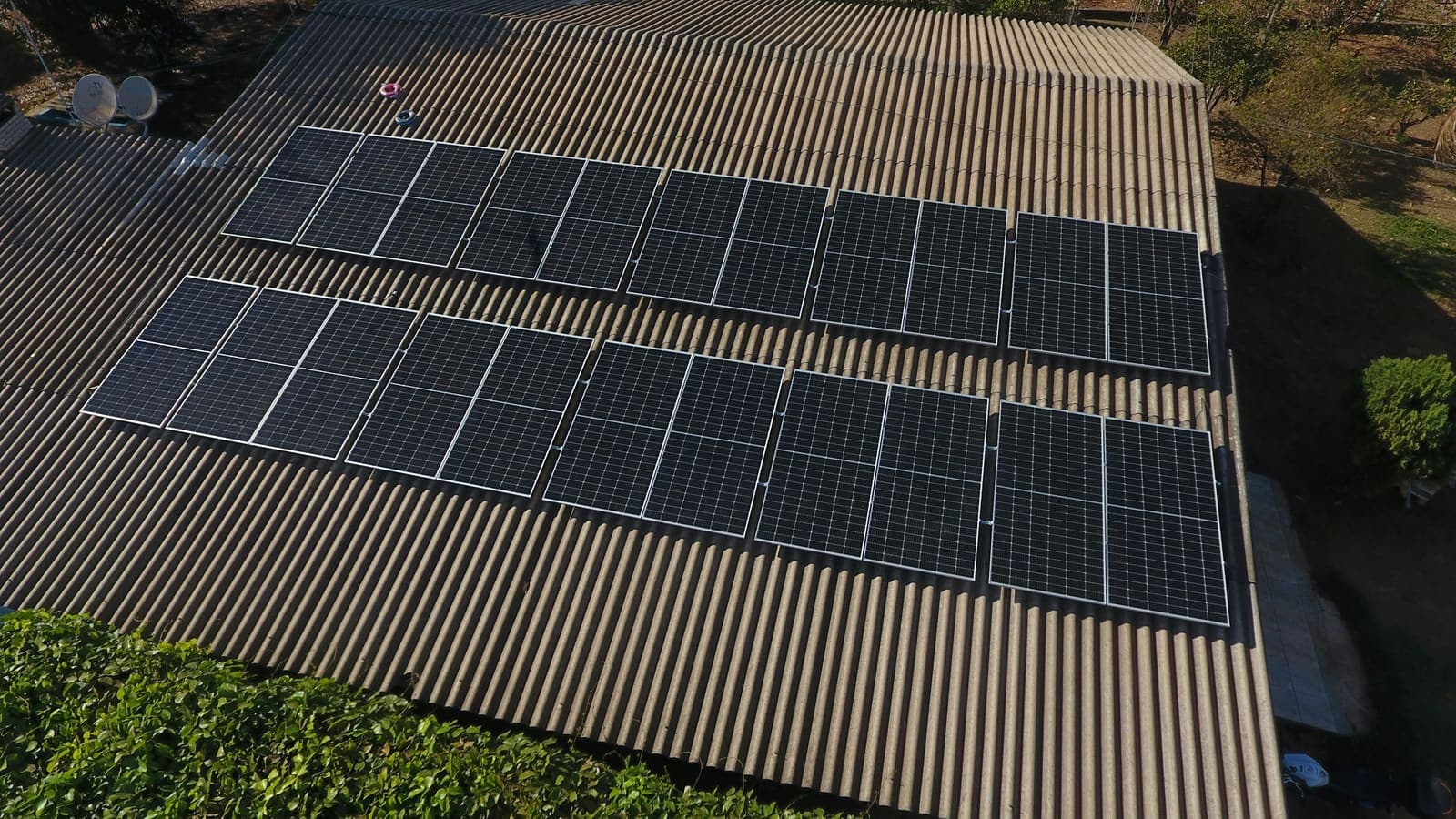 Aerial view of a corrugated roof with two rows of solar panels, trees along one side